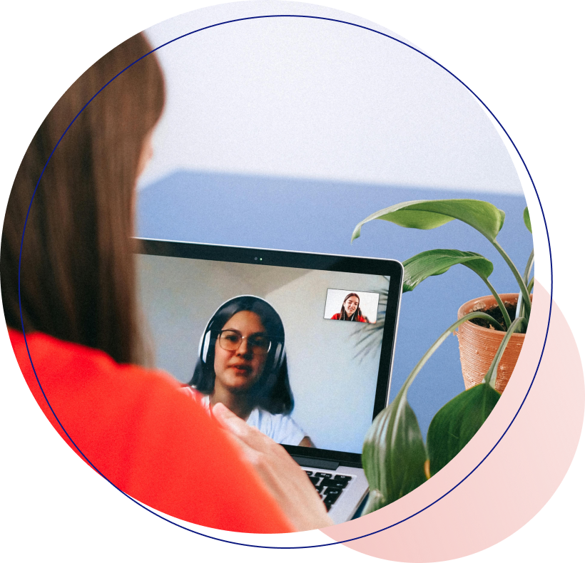 Tutor Development Photo taken of over a woman's shoulder who is talking to a medium-light skin toned woman wearing headphones on a laptop video chat